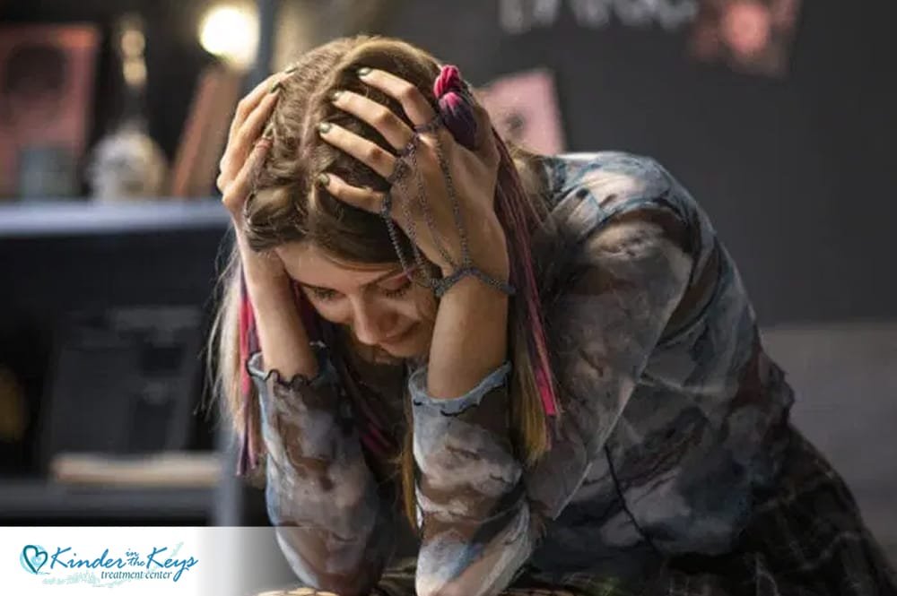 Teen girl sitting with her head in her hands, looking distressed, possibly experiencing emotional stress or symptoms related to narcissistic abuse.