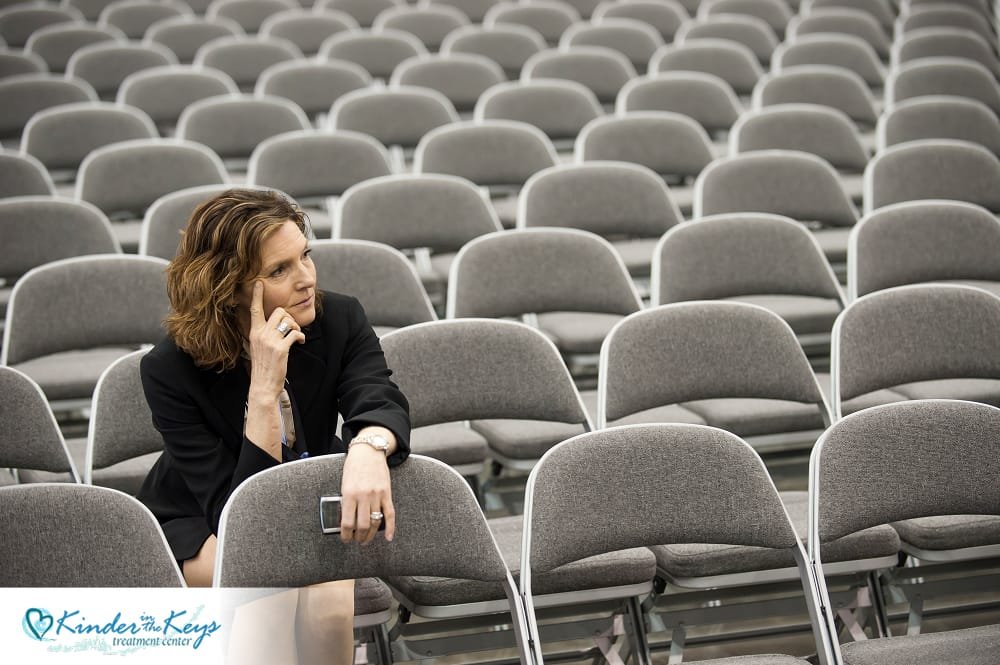 A woman in an event theatre alone surrounded by empty chairs signifying her loneliness and depression