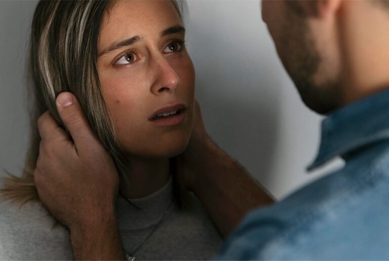 Close-up of a frightened woman with a man's hands gripping her face, depicting fear and emotional abuse.