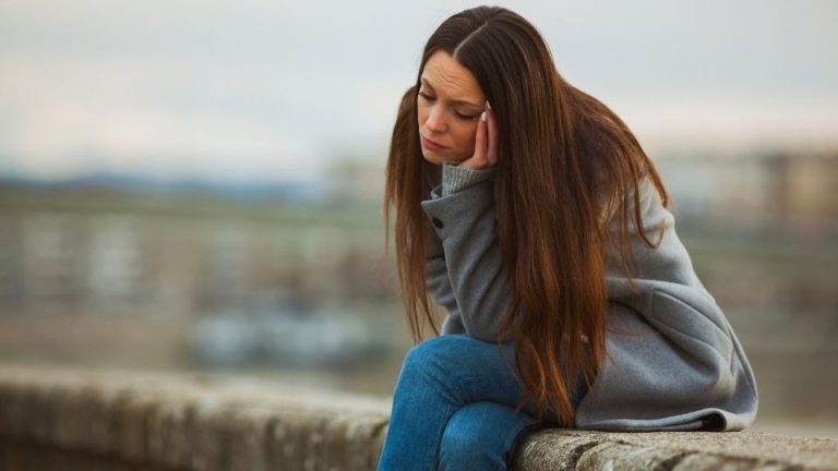 Smiling Depression Signs You're Hiding Depression Behind a Smile hero image of a woman hiding the pain.