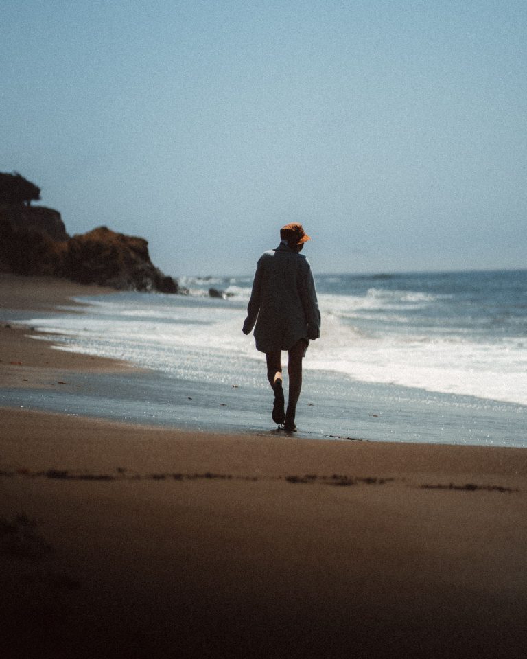 A woman walking peacefully along the shoreline during narcissistic abuse recovery for women