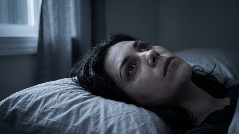 Woman lying awake at night after a PTSD nightmare, unable to fall back asleep.